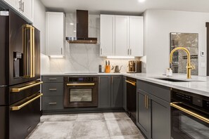 Une cuisine moderne avec des meubles de couleur sombre, des appareils en acier inoxydable et un plan de travail en marbre.