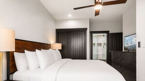 Quarto com cama, mesa de cabeceira, cômoda, ventilador de teto e porta para o banheiro.