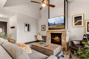 A living room with a fireplace, a mounted TV, and a ceiling fan. - Crystal Peak Lodge 7404 ~ Ski-in/Ski-out ~ NEW LISTING ~ By CoralTree Residences (Breckenridge)