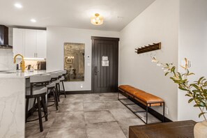 A modern kitchen with a marble countertop, bar stools, a bench, and a door with a dark frame. - Crystal Peak Lodge 7404 ~ Ski-in/Ski-out ~ NEW LISTING ~ By CoralTree Residences (Breckenridge)