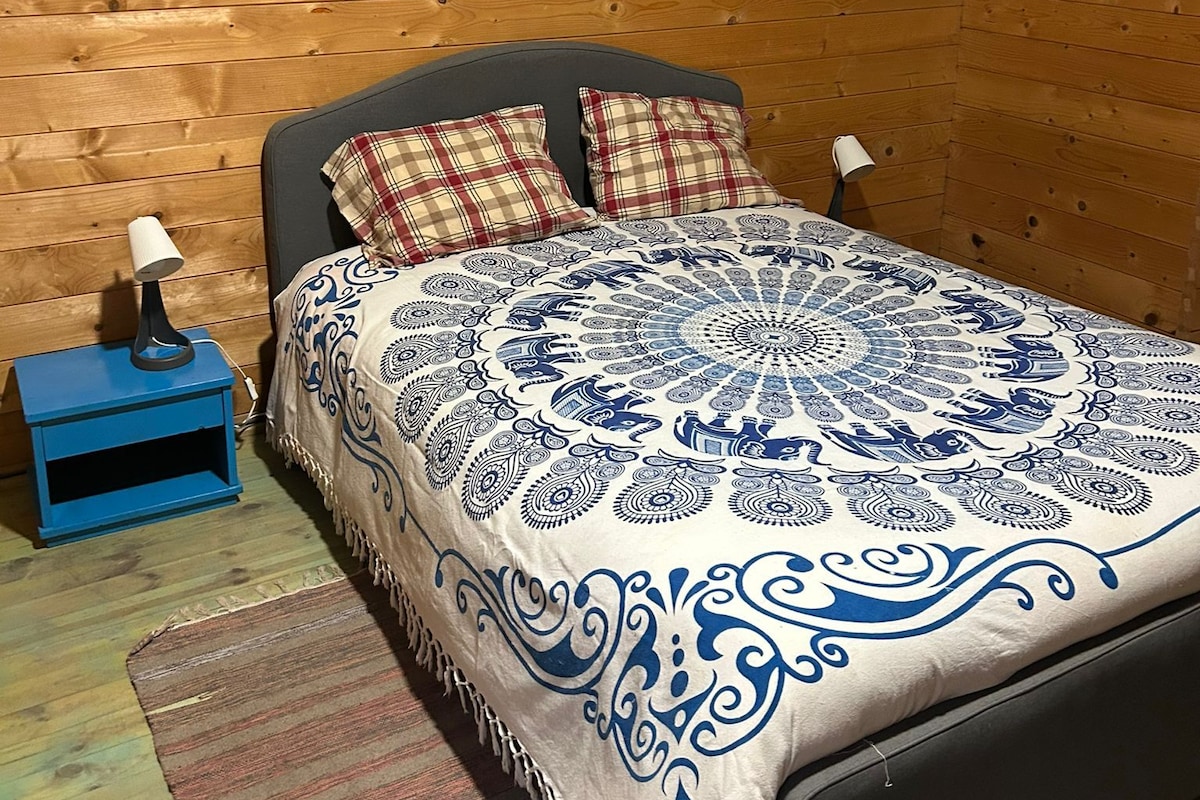 Un dormitorio tipo cabaña de madera con una cama, dos almohadas, una mesita de noche y una lámpara.