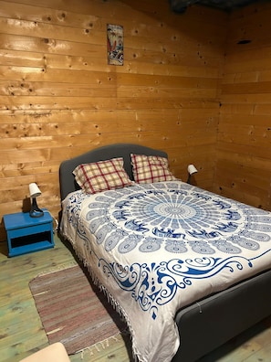 Un dormitorio tipo cabaña de madera con una cama, dos almohadas, una mesita de noche y una lámpara.
