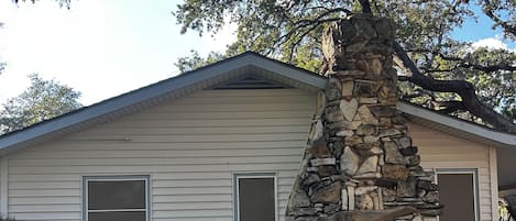 A single-story house with a stone pillar, a black metal fence, and a grassy yard.