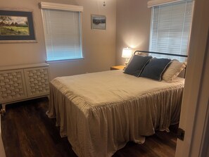 A bedroom with a bed, two windows with blinds, a nightstand with a lamp, and a wall-mounted picture. -  Lake Granbury Waterfront Cottage! 2 miles from Downtown with private boat dock! (Granbury)