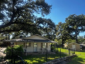 A single-story house with a front porch, surrounded by a stone wall and a metal fence.