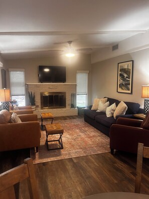 A living room with a fireplace, sofas, a television, and a painting on the wall. -  Lake Granbury Waterfront Cottage! 2 miles from Downtown with private boat dock! (Granbury)