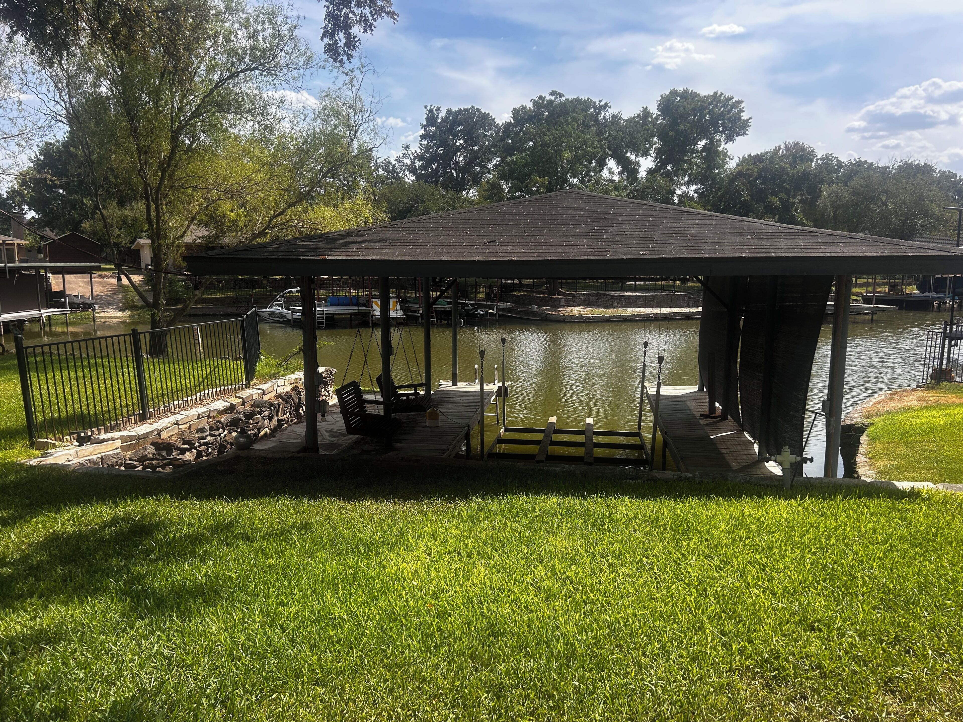 Ein Pavillon mit einer Anlegestelle über Wasser, umgeben von Gras und Bäumen.