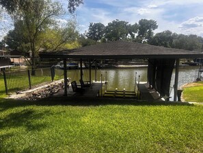 Ein Pavillon mit einer Anlegestelle über Wasser, umgeben von Gras und Bäumen.