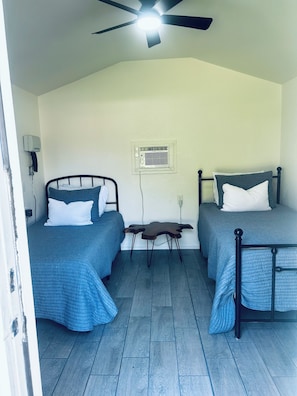 Une chambre avec deux lits, un ventilateur de plafond, un appareil de climatisation et une petite table.