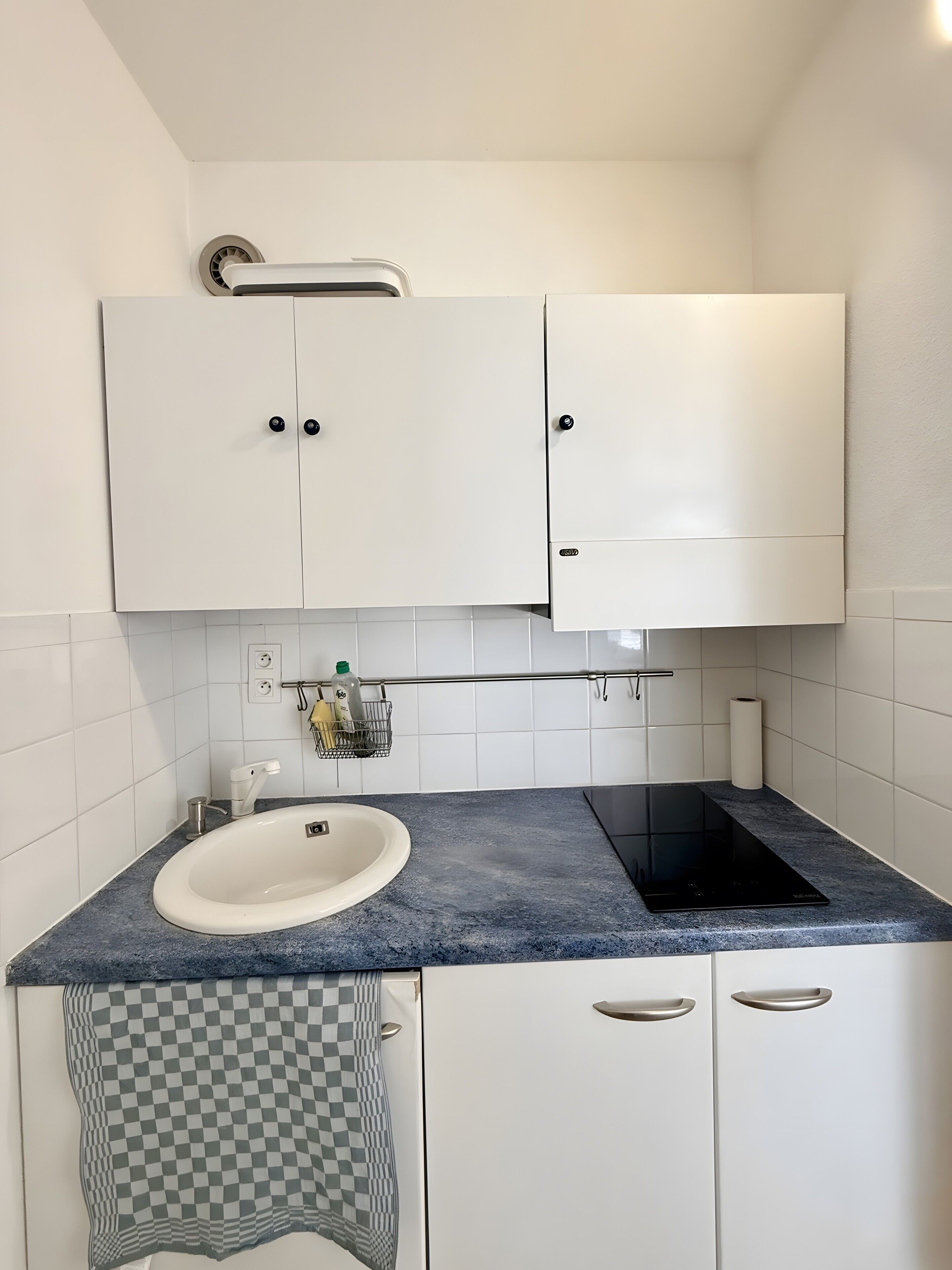 Un baño moderno con un lavamanos blanco, una cocina de inducción negra y armarios blancos.