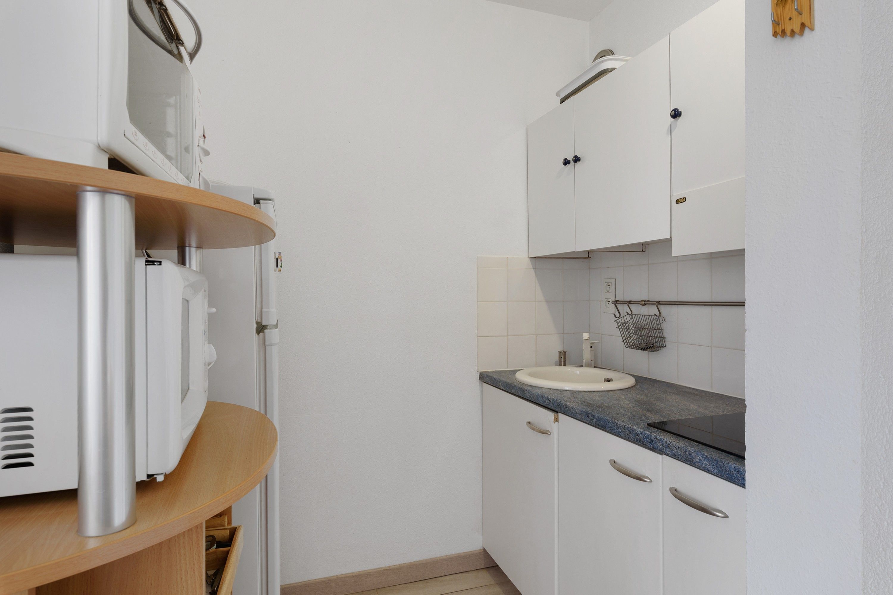 A compact kitchen with white cabinets, a granite countertop, and a built-in oven.