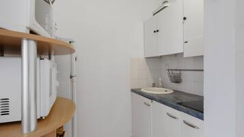 A compact kitchen with white cabinets, a granite countertop, and a built-in oven.