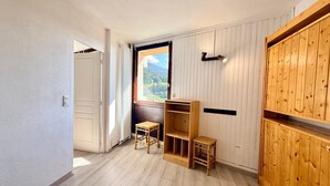 Une pièce avec une armoire en bois, une fenêtre donnant sur une montagne et un petit tabouret en bois.