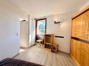 Ein Zimmer mit einem Holzschrank, einem Fenster mit Bergblick und einem kleinen hölzernen Hocker.