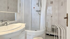Une salle de bain avec une douche à parois incurvées, un lavabo blanc doté d’un plan de toilette en marbre et un petit tabouret.