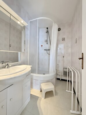Ein Badezimmer mit einer Duschkabine mit Bogenform, einem weißen Waschbecken mit Marmorplatte und einem kleinen Hocker.