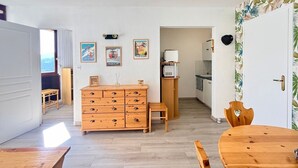 Un espace de vie compact comprenant une commode en bois, une table à manger et un coin cuisine.