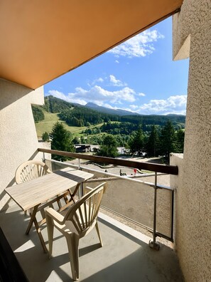 Ein Balkon mit Tisch und Stühlen, der auf eine grüne Landschaft mit Bäumen und einer Straße blickt.