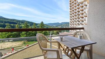 Een balkon met een tafel en stoelen, met uitzicht op een bergachtig landschap.