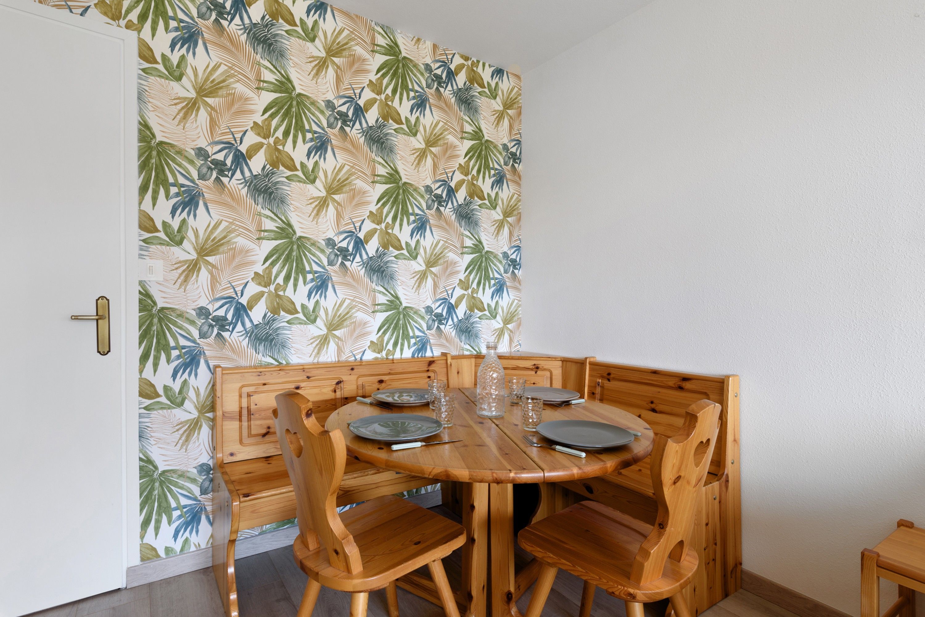 Un coin repas avec une table et des chaises en bois, un mur orné d’un motif et une porte dotée d’une poignée en laiton.