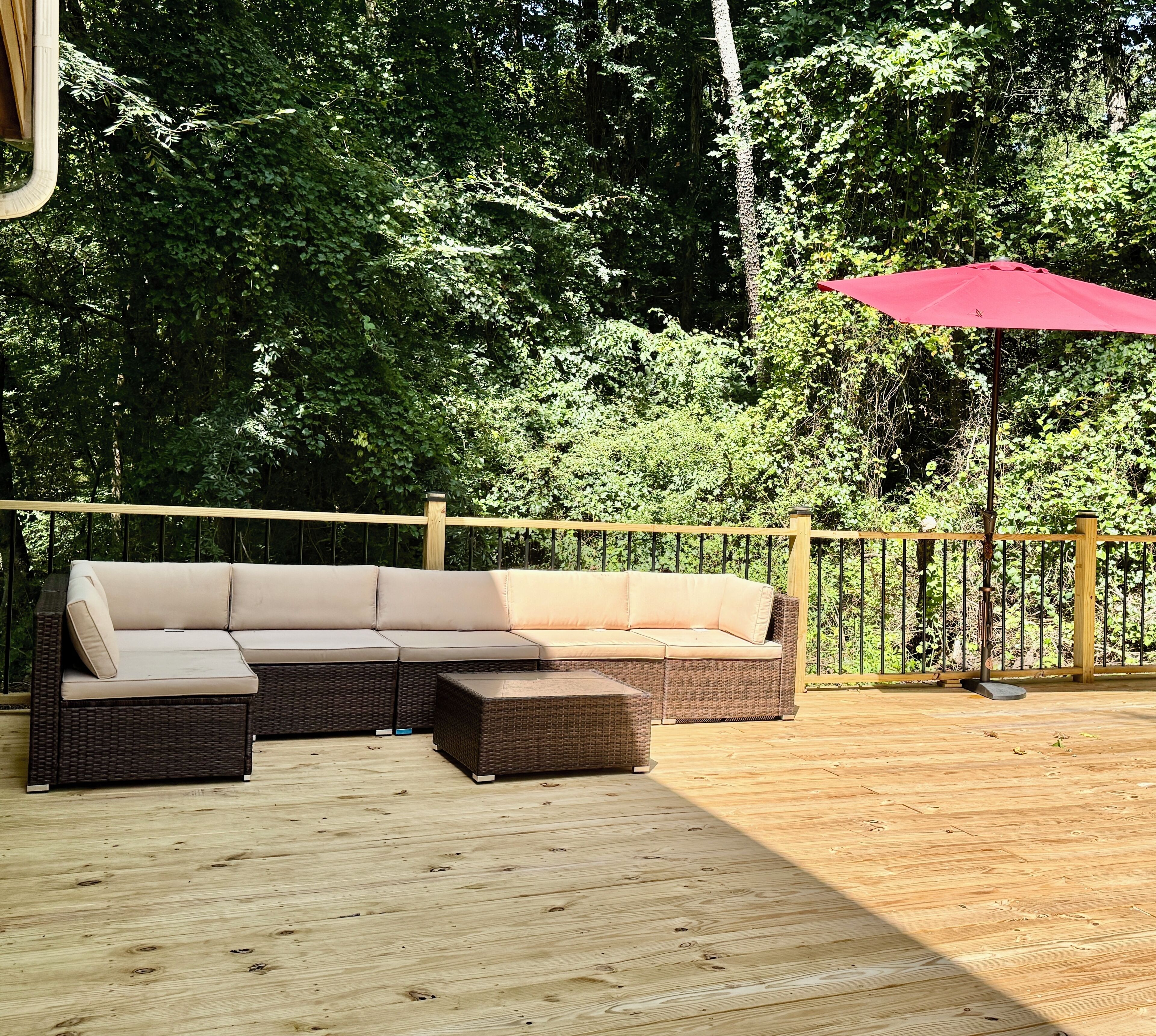 A wooden deck with a sectional sofa and a red umbrella.