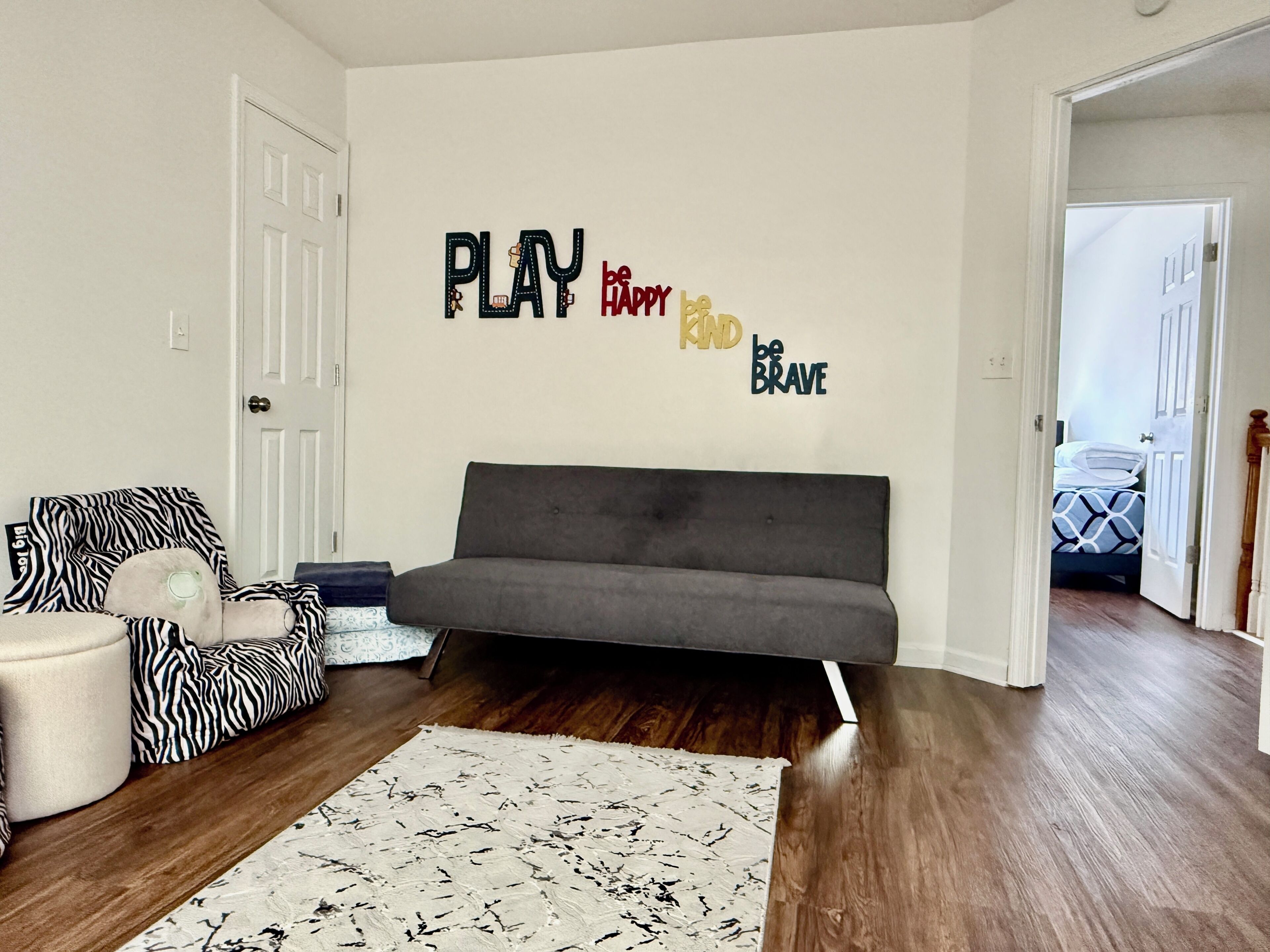 A living room with a grey sofa, a zebra-patterned couch, a white rug, and motivational wall art.