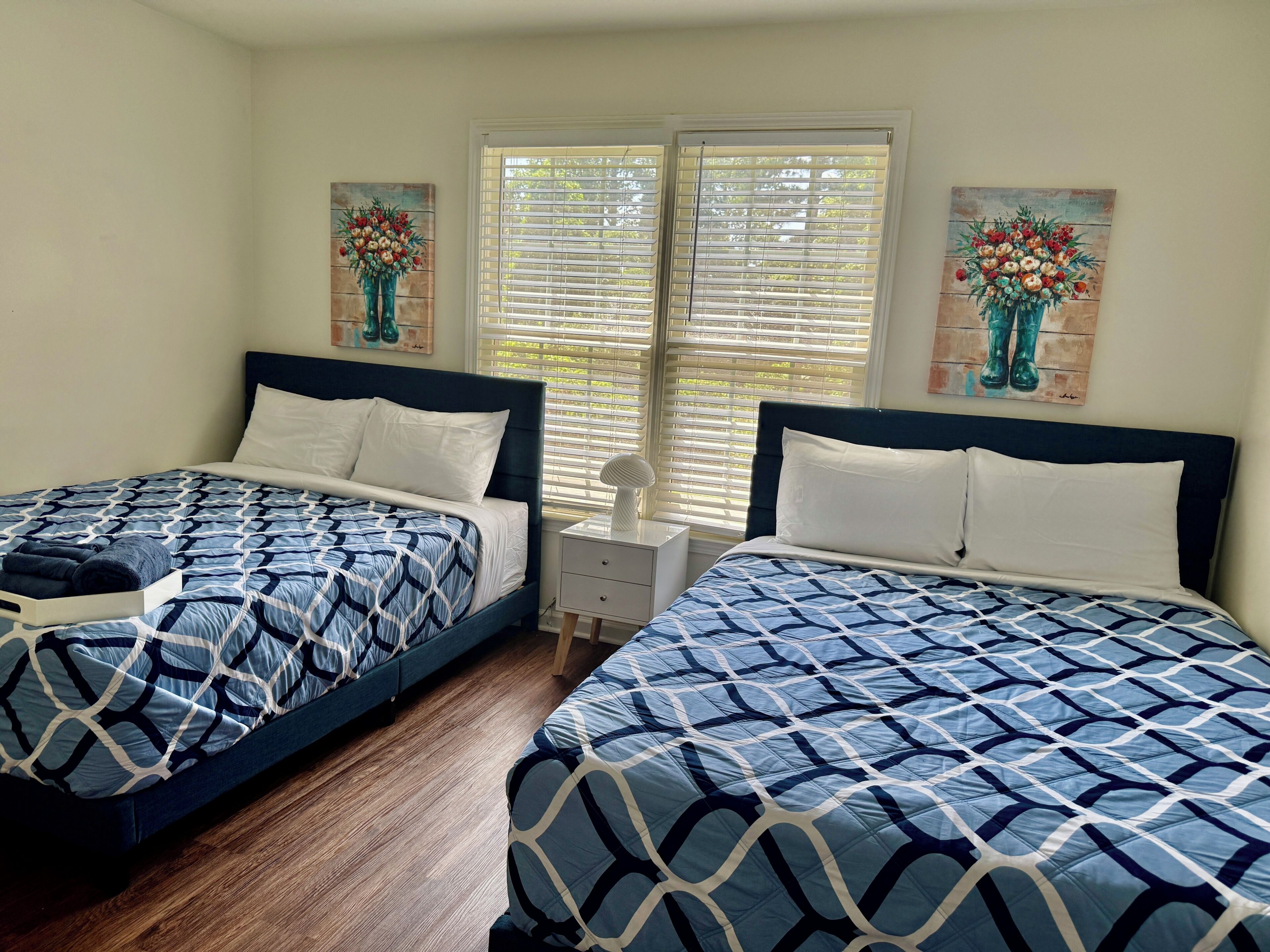 A bedroom with two beds, a nightstand, and a window with blinds.