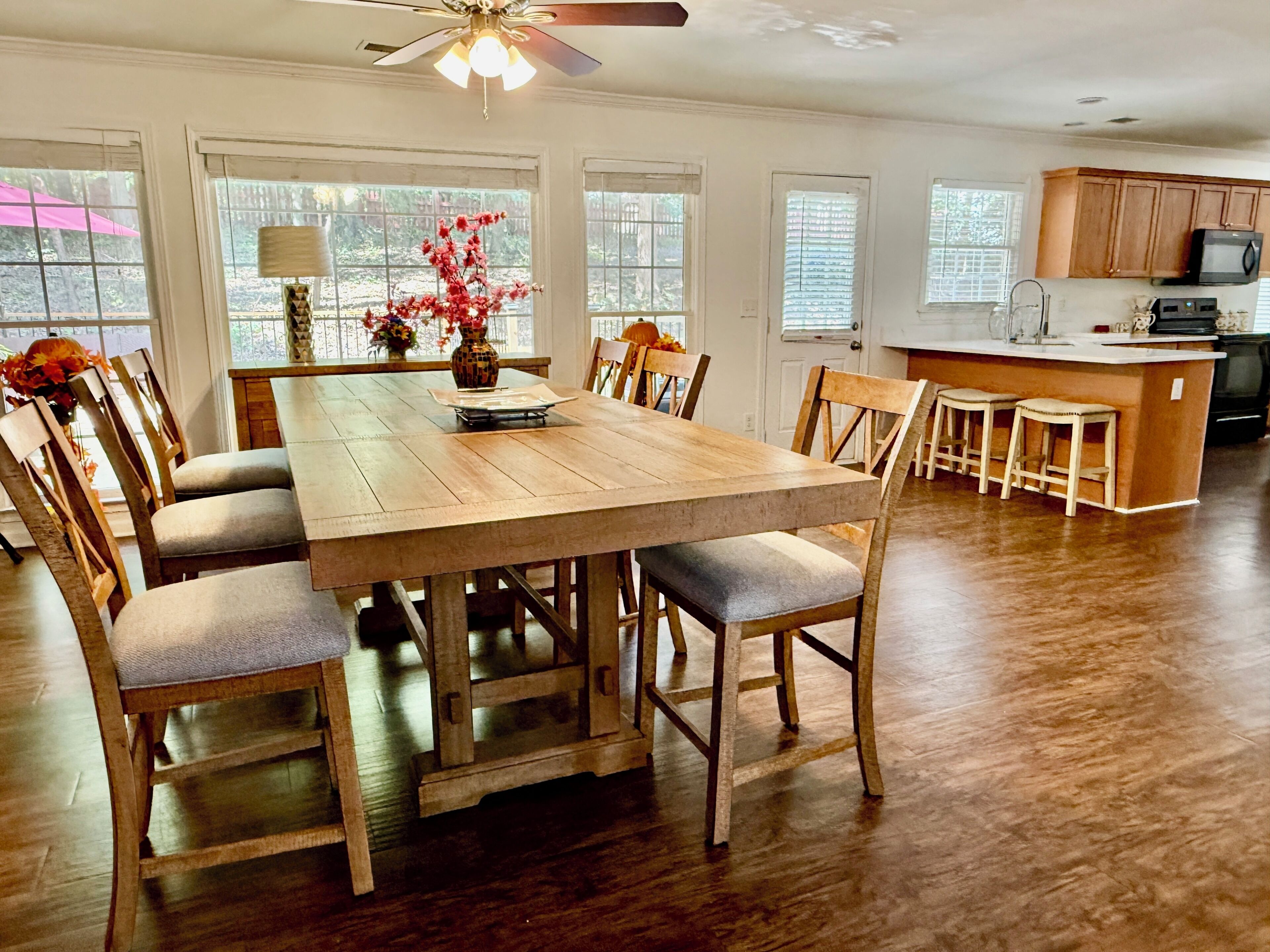 A dining area with a wooden table and chairs, a ceiling fan, and a kitchen in the background.