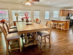 Un coin repas avec une table et des chaises en bois, un ventilateur de plafond et une cuisine en arrière-plan.