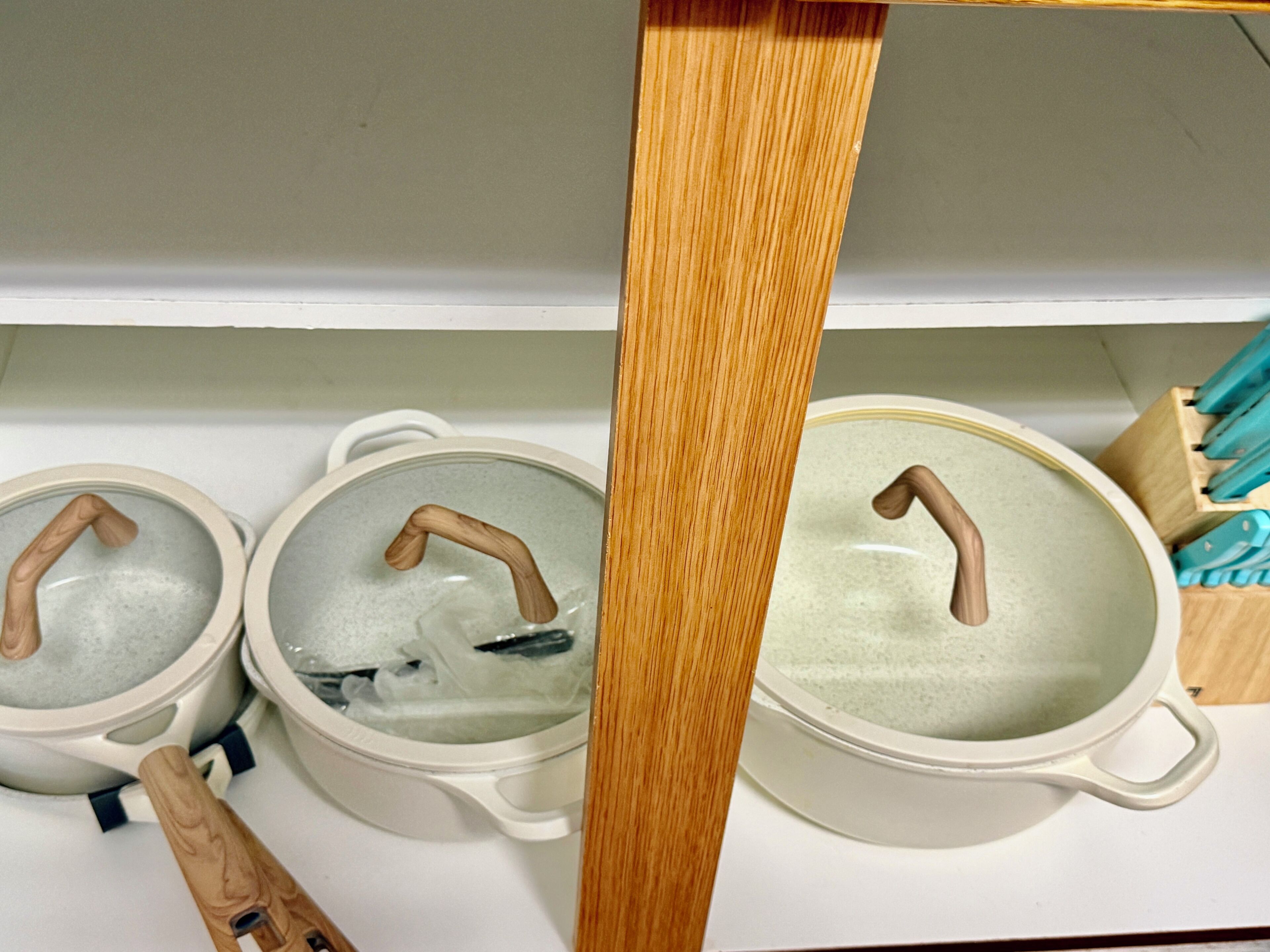 Trois pots en céramique blanche, dotés d’anses en bois, sont posés sur un comptoir blanc.