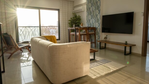 A modern living room with a sofa, a coffee table, a TV, and a balcony with a view. - Cozy & Bright 2-Room Apartment in Dakar (Dakar)