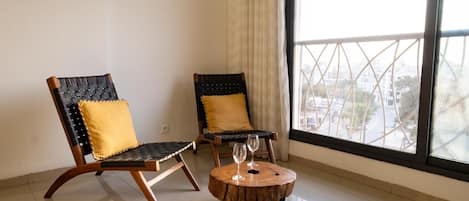 A room with two chairs, a round wooden table, and a large window with a view of buildings.