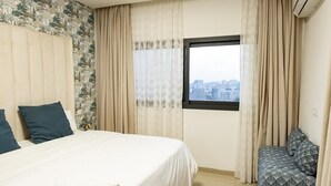 A hotel room with a bed, a bench, and a window with a city view. - Cozy & Bright 2-Room Apartment in Dakar (Dakar)