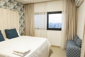 A hotel room with a bed, a bench, and a window with a city view. - Cozy & Bright 2-Room Apartment in Dakar (Dakar)