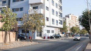 A multi-story residential building with balconies, a clear sky, and a street with cars and pedestrians. - Cozy & Bright 2-Room Apartment in Dakar (Dakar)