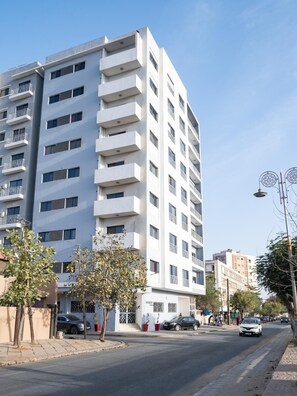 A multi-story residential building with balconies, a clear sky, and a street with cars and pedestrians. - Cozy & Bright 2-Room Apartment in Dakar (Dakar)