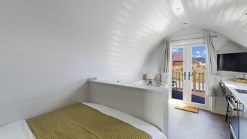 A bedroom with a bed, a desk with a chair, a window with curtains, and a view of the outside.