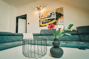 Ein modernes Wohnzimmer mit einem grauen Sofa, einem weißen Couchtisch mit einem schwarzen Drahtkorb und einer Vase mit Blumen.