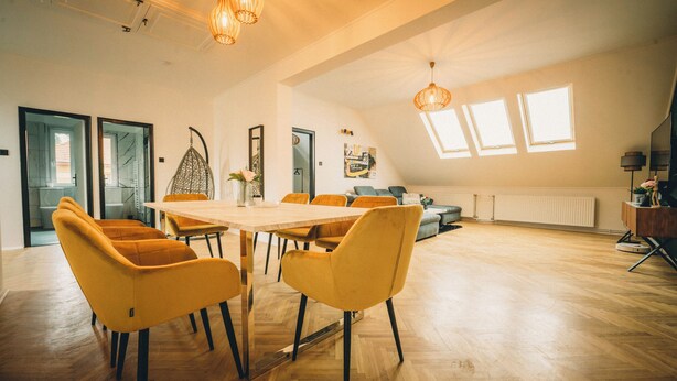 A spacious room with a large wooden table and yellow chairs, a sofa, and a ceiling light fixture. - Modern 4-bedroom vacation rental with a garden in Siófok; dog-friendly (Siófok)