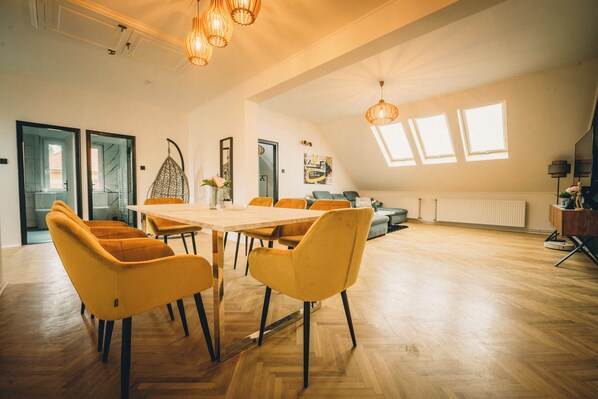 A spacious room with a large wooden table and yellow chairs, a sofa, and a ceiling light fixture. - Modern 4-bedroom vacation rental with a garden in Siófok; dog-friendly (Siófok)