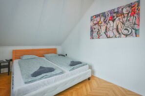 Ein Zimmer mit einem Bett, einem Nachttisch, einem kleinen Tisch und einem farbenfrohen, abstrakten Gemälde an der Wand.