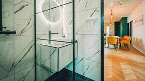 A modern bathroom with a glass-enclosed shower, a marble-tiled wall, and a round mirror. - Modern 4-bedroom vacation rental with a garden in Siófok; dog-friendly (Siófok)