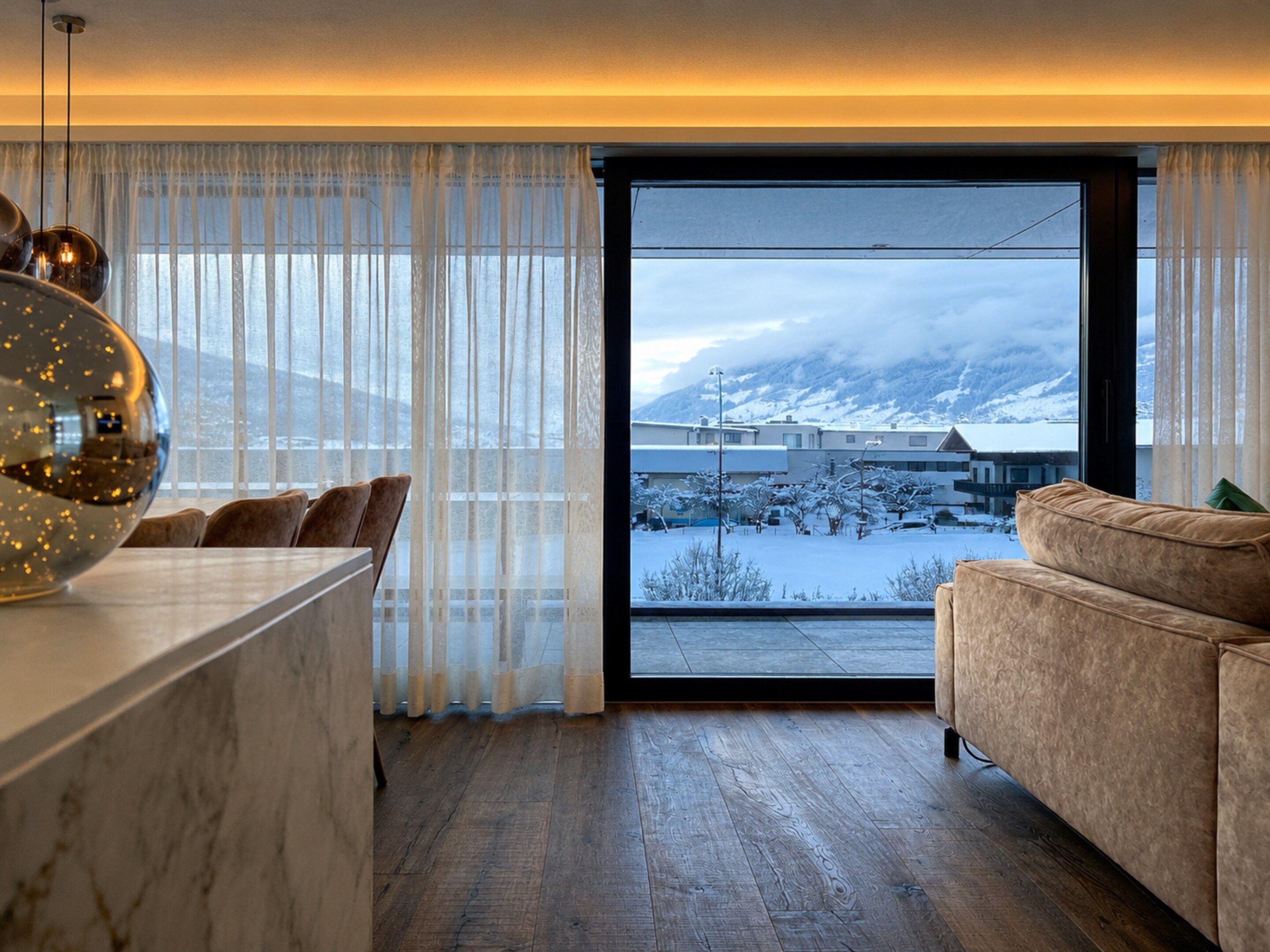Una sala de estar moderna con un ventanal grande, piso de madera y vista a un paisaje nevado.