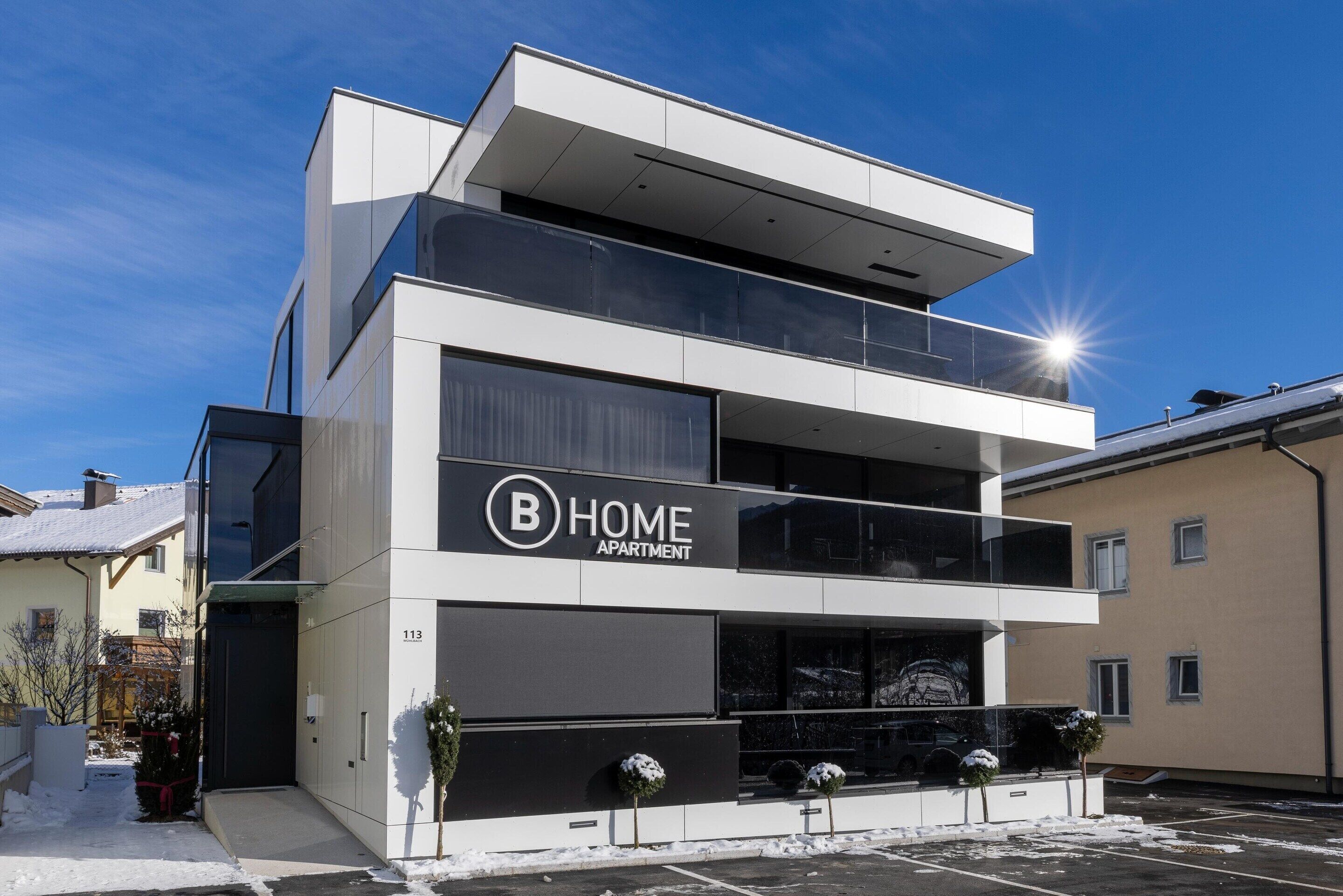 Un moderno edificio de apartamentos de dos pisos con un letrero llamativo que dice 'B HOME APARTMENT'.