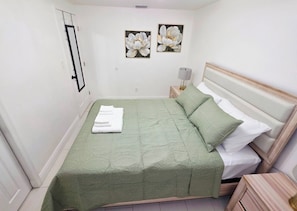 A neatly made bed with a green bedspread and white pillows, a bedside lamp, and two framed floral paintings on the wall. - Family Pool Retreat - Sleeps 8 - Pet Friendly (Tampa)