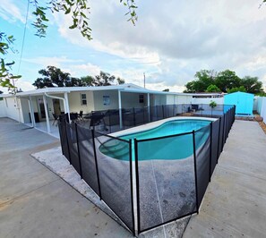 A swimming pool with a surrounding fence, a covered patio area with chairs, and a blue shed in the background. - Family Pool Retreat - Sleeps 8 - Pet Friendly (Tampa)