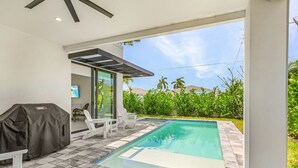 Une piscine avec un espace patio, du mobilier d’extérieur et un barbecue couvert.