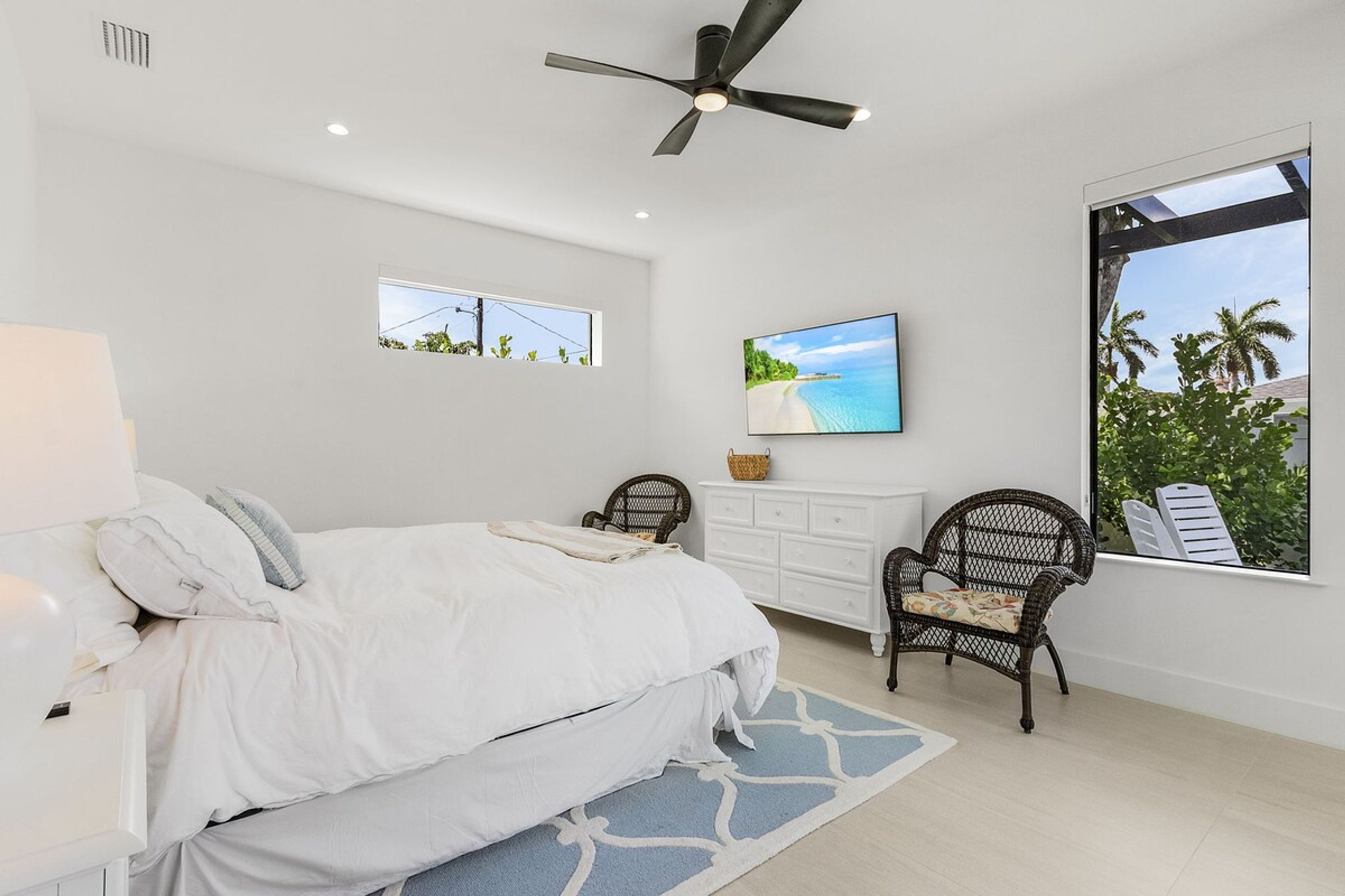 A bedroom with a bed, a chair, a dresser, and a large window with a view.