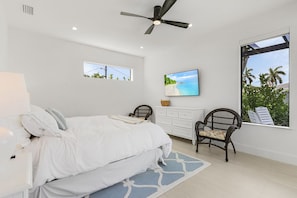 Un dormitorio con cama, una silla, tocador y un ventanal con vistas.