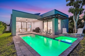 Una casa moderna con piscina, mobiliario exterior y un patio cubierto.